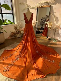 an orange dress is on display in front of a mirror and flower arrangements are behind the mannequin