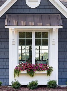 a blue house with two windows and flowers in the window boxes on the front porch