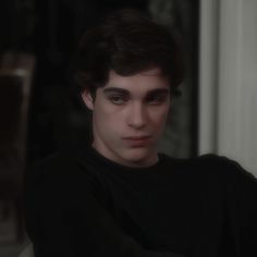 a young man with dark hair is staring at the camera while wearing a black shirt