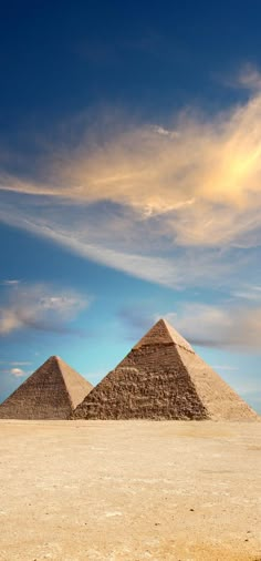 three pyramids in the desert under a cloudy sky