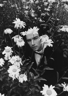 a man is hiding in the middle of some daisies with his face hidden behind him