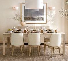 a dining room table with white chairs and an art piece on the wall above it