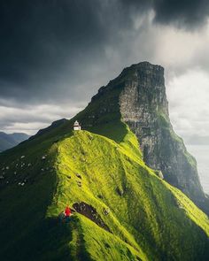 a green hill with a house on top and dark clouds in the sky above it