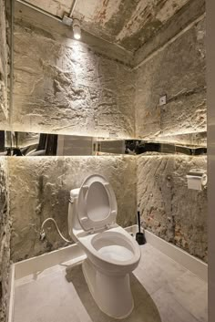 a white toilet sitting inside of a bathroom next to a stone wall with mirrors on it