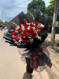 a woman is walking down the street holding a bouquet of red roses and greenery