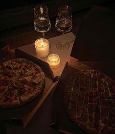 two pizzas sitting next to each other on top of a table with candles in front of them