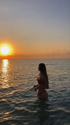 a woman standing in the water at sunset