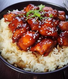 a black bowl filled with rice and meat covered in sesame seeds on top of a wooden table