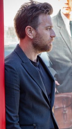 a man standing next to a red pole in front of a movie poster and holding a briefcase