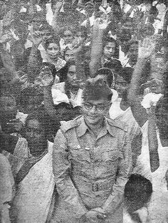 an old black and white photo of a man standing in front of a large group of people