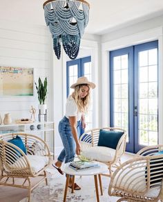 a woman standing in a living room next to some chairs and a chandelier