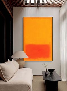 a living room with a couch, coffee table and large orange painting on the wall