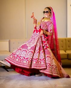 a woman in a pink and red bridal gown posing for the camera with her hand up