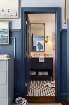 an open door leading to a bathroom with blue walls and tile flooring, along with pictures on the wall