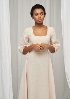 a woman standing in front of white curtains wearing a dress with puffy sleeves and a square neckline