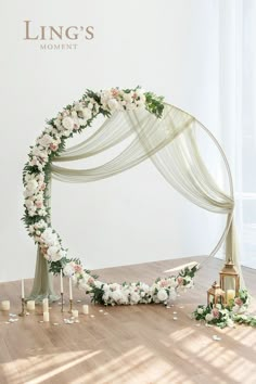 a wedding arch decorated with white flowers and greenery on the floor next to candles