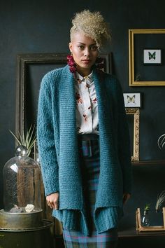 a woman standing in front of a wall wearing a blue cardigan and plaid skirt