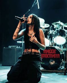 a woman sitting on the ground while holding a microphone in her hand and singing into a mic