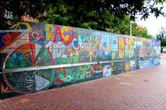 a wall covered in graffiti on the side of a building next to a brick sidewalk