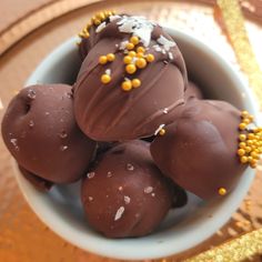 four chocolate balls in a bowl with sprinkles on the top and gold trim around them