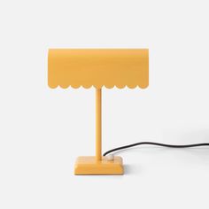 a yellow lamp on a white surface with a cord attached to the base and an electric plugged into it