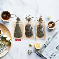 three bags of tea sitting on top of a table next to cups and spoons