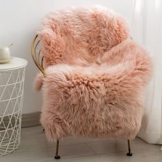 a chair with a pink fur on it next to a white vase and window sill