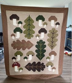 a quilted wall hanging with trees and mushrooms on it