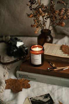 a candle sitting on top of a book next to a vase filled with flowers and leaves