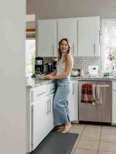 a woman standing on the kitchen counter in front of the sink and dishwasher