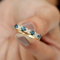 a woman's hand holding a gold ring with blue and white stones