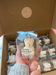 a person holding up a small teddy bear in a box with other items behind it