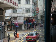 a red car driving down a street next to tall buildings and people walking on the sidewalk