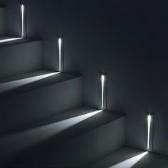 three lights that are on the side of a set of stairs in an empty room