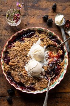 a bowl filled with ice cream and fruit on top of a wooden table next to spoons