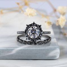 a black and white diamond ring sitting on top of a marble slab with flowers in the background