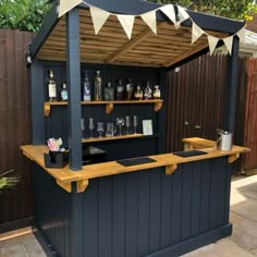 an outdoor bar with bottles and glasses on the top shelf, next to a fence