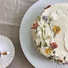 a cake with white frosting and flowers on it next to a cup of coffee