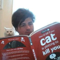 a man reading a book with a cat sitting on top of his head next to him