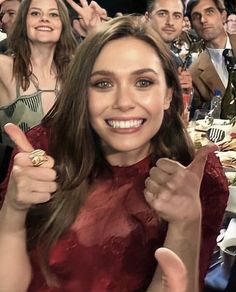 a woman in a red dress is giving the peace sign with her hands and smiling