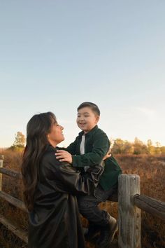 a woman holding a young boy on top of a wooden fence