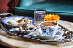 a cup of coffee and some cookies on a tray with a flower in the middle