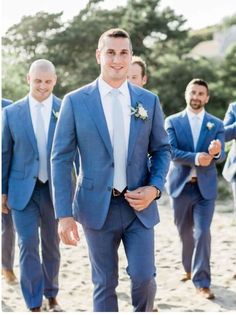 a man in a blue suit and white shirt is walking down the beach with other men