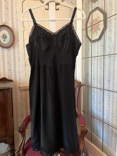 This is a beautiful, medium weight, satiny feeling polyester black slip or slip dress, trimmed with black lace on the bust and bottom edge. The measurements, taken with the slip lying flat, are: armpit to armpit/bust, 19 inches; waist, 17 inches; length, 41 inches (from top of strap); bottom edge, 28 inches. In very good condition. Black Satin Camisole With Lace Trim, Black Dress With Bias Cut And Spaghetti Straps, Black Bias-cut Dress With Spaghetti Straps, Black Bias Cut Dress With Spaghetti Straps, Black Slip Dress With Contrast Lace, Black Lace Trim Spaghetti Strap Camisole, Black Dress With Built-in Bra For Night, Elegant Black Slip Dress With Contrast Lace, Elegant Black Slip Dress With Lace Trim