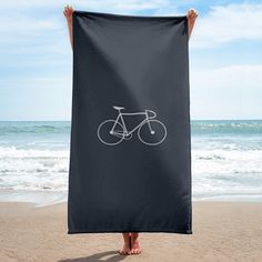 a person holding up a towel with a bicycle drawn on it in front of the ocean