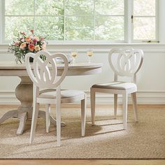 two white chairs sitting at a table with flowers in the vase on top of it