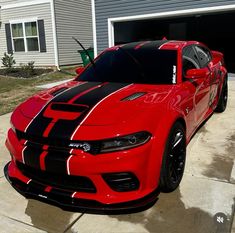 a red car with black stripes parked in front of a garage on the side of a house