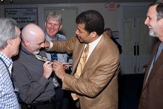 a group of men standing next to each other in a room with one man tying another mans tie