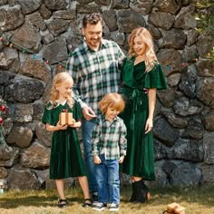 a man, woman and two children standing in front of a stone wall holding presents