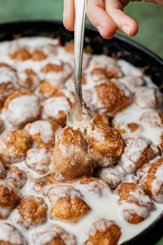 a person is spooning some sugared doughnuts into a pan with milk